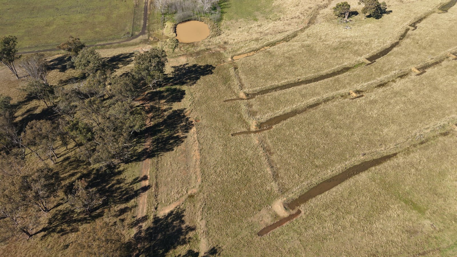 Parallel water-filled earthworks, a dam and trees seen from above.