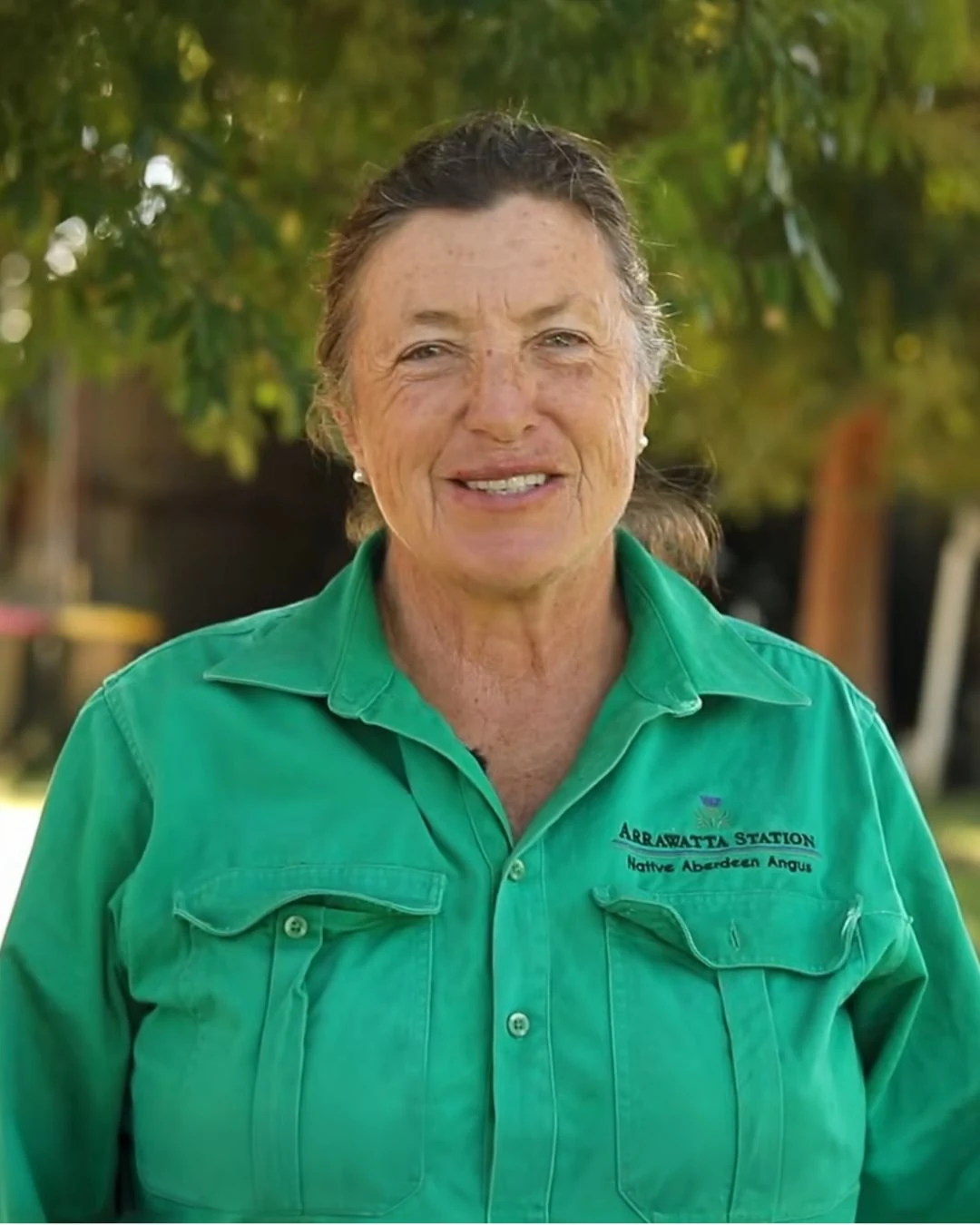 Susan Hendry outdoors in a green Arrawatta work shirt, with cattle yards behind her.